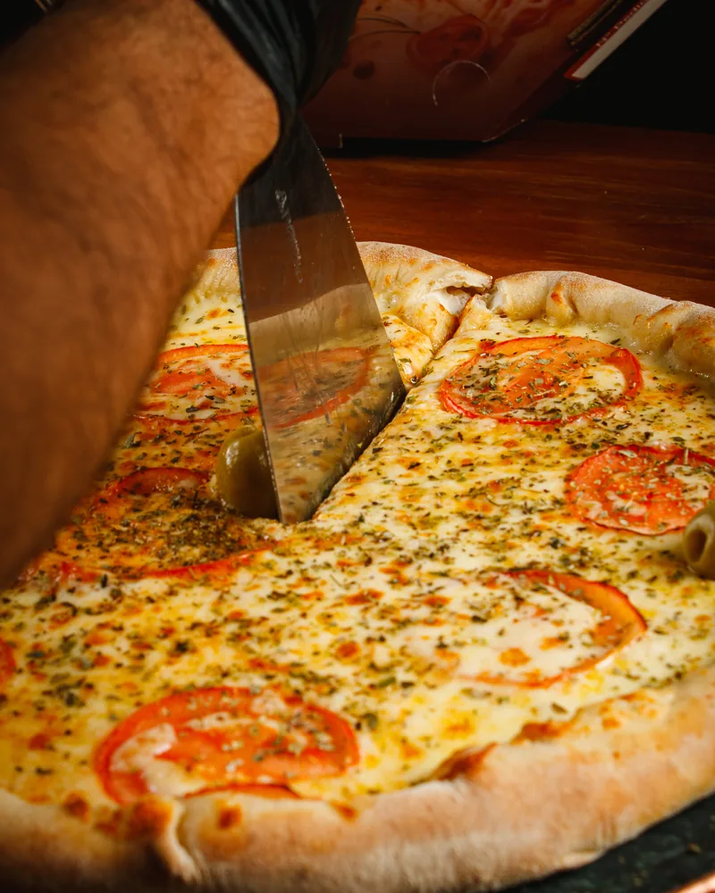Fatia de pizza sendo servida, massa artesanal e borda dourada