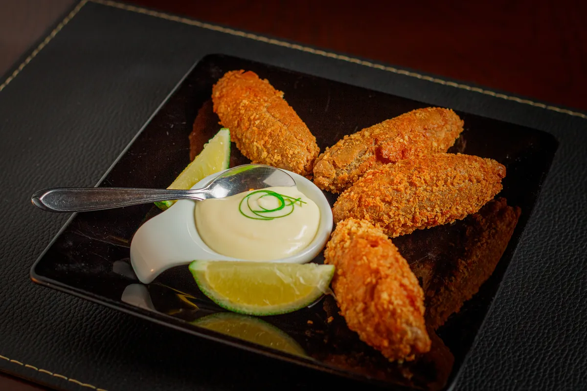 Croquetes empanados no prato preto com limão e molho